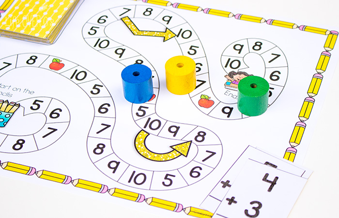 Students play the addition to 10 board game by drawing an addition card, solving it, and moving their game piece to that number on the game path.