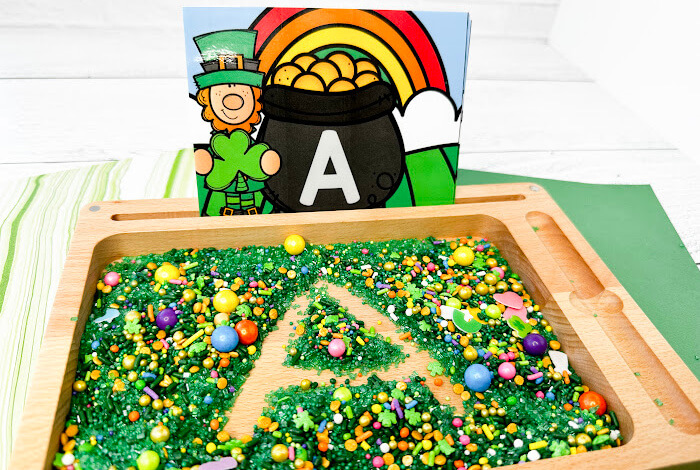 St. Patrick's Day writing tray with green sprinkles and St. Patrick's Day marshmallow theme sprinkles. The letter A sample card is shown and the letter A is traced into the sprinkles